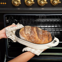 Baked sourdough batard being taken out of the oven in the oval bread cloche