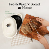 Sliced bread on a board beside the open oval bread oven with its steam-circulating lid