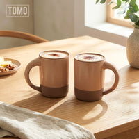 Two Wheat stoneware mugs with coffee on a wooden table by a window