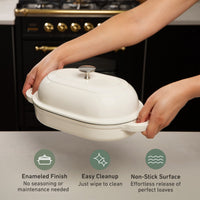 Hands lifting the domed lid of the oval bread oven: enameled finish, easy cleanup, non-stick surface