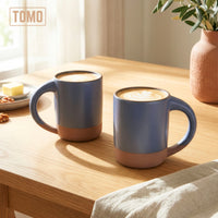 Two Harbor Blue stoneware mugs with coffee on a wooden table by a window