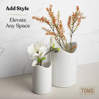 The two ceramic utensil crocks used as vases with orange branches and a white flower
