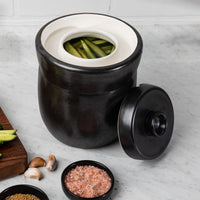 Looking down into the 7L crock's white glazed interior with cucumbers fermenting, lid resting beside it