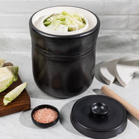3L crock open and packed with shredded cabbage, with the lid, wooden tamper and ceramic weights alongside