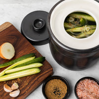 Cucumbers, onion and spices packed into the water-seal crock on a wooden board, lid off
